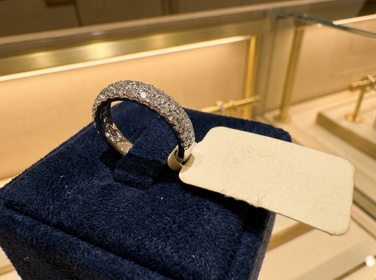 A finished pave diamond ring displayed on a navy velvet tray at a jewelry counter, with a blank presentation tag beside it