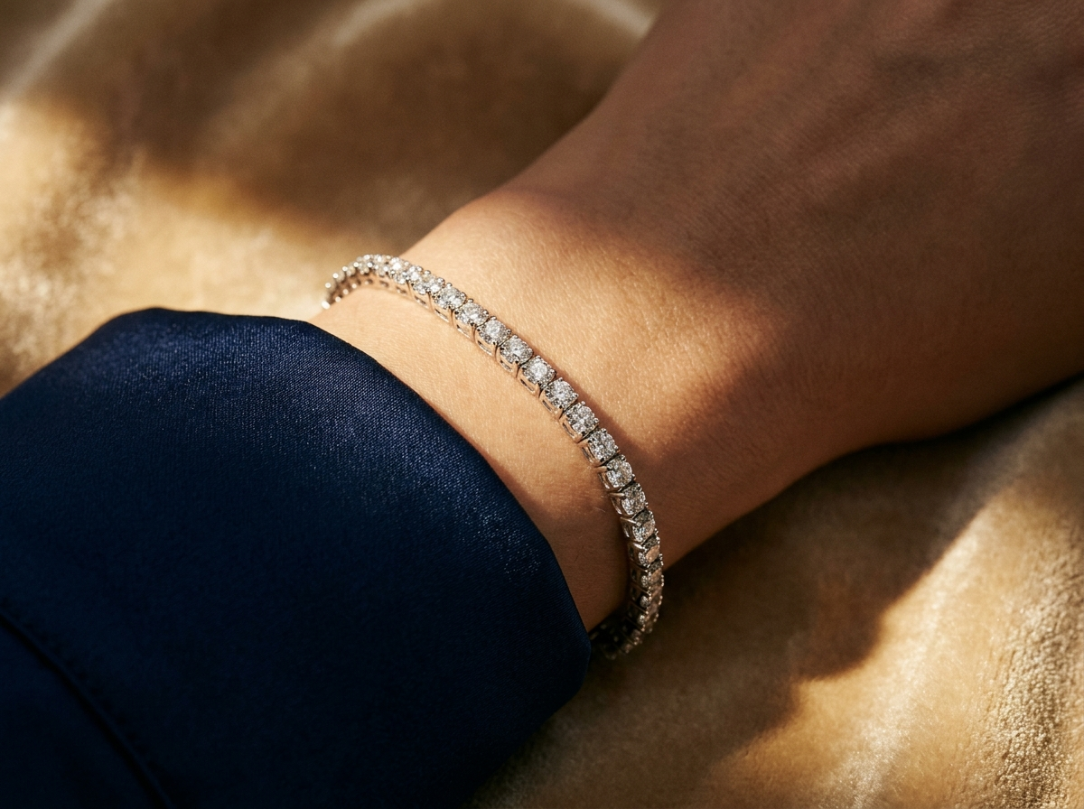 Close-up of a finished natural diamond tennis bracelet showing uniform color and clarity across a continuous prong-set line, navy and gold trade editorial style
