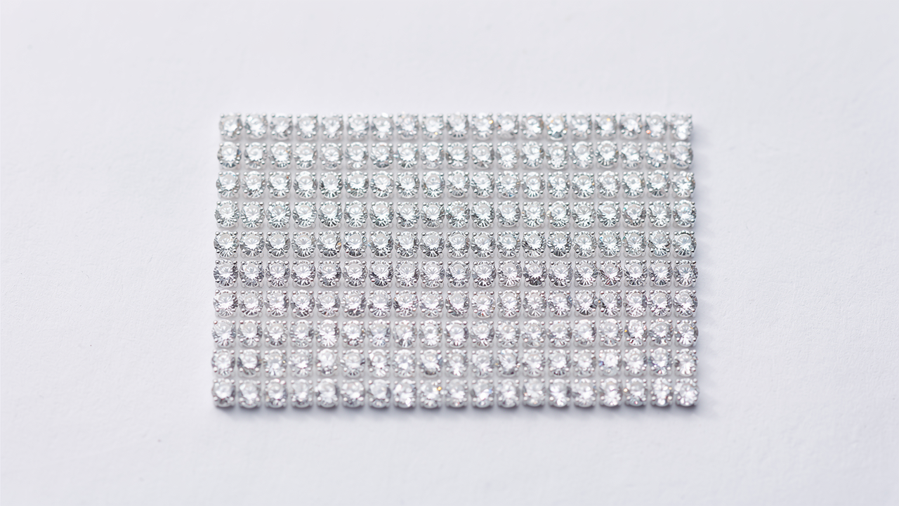 Neat rows of tiny calibrated melee diamonds arranged in white parcel paper folds in a precise grid on a white table
